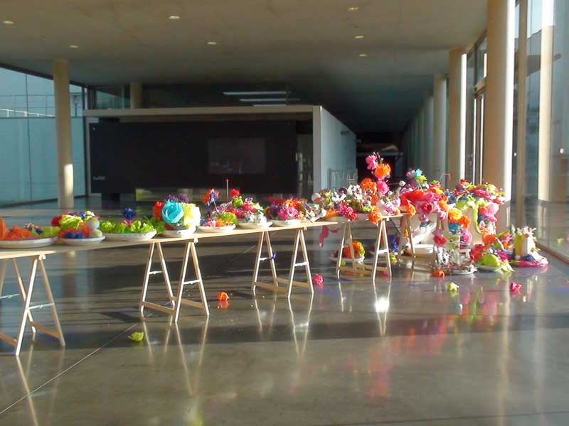une table de 10 mètres de long, potée par des tréteaux, en travers du hall d'accueil du MAC/VAL, musée d'art contemporain du Val-de-Marne. Dessus sont posés des plats ronds ou ovales en polystyrène expansé qui débordent de fleurs en papier de couleurs vives.