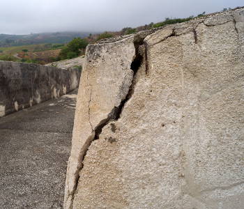 Un profonde fissure entaille l'angle d'une muraille au coin d'une ruelle dans un paysage de collines sous un ciel bas
